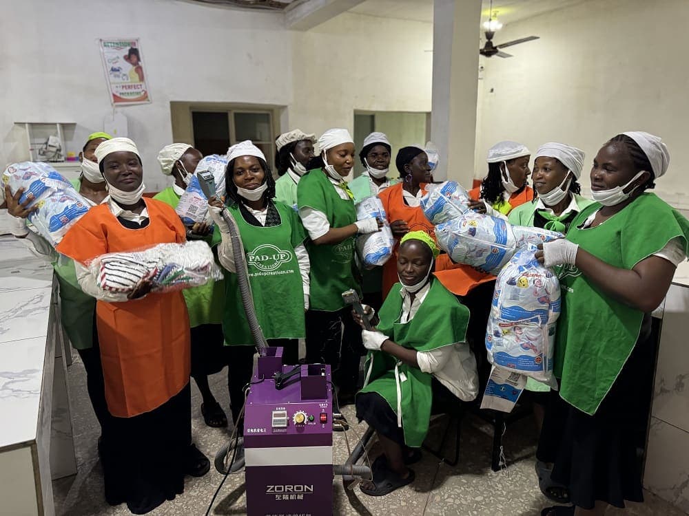 Pad-Up production staff on the factory floor holding finished packs beside a sealing machine